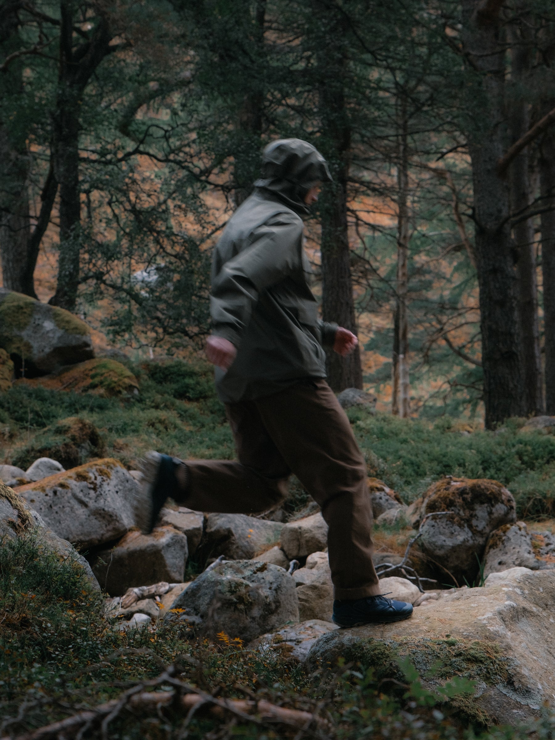 A man running through a forest in the Cairngorms, wearing a waterproof jacket.