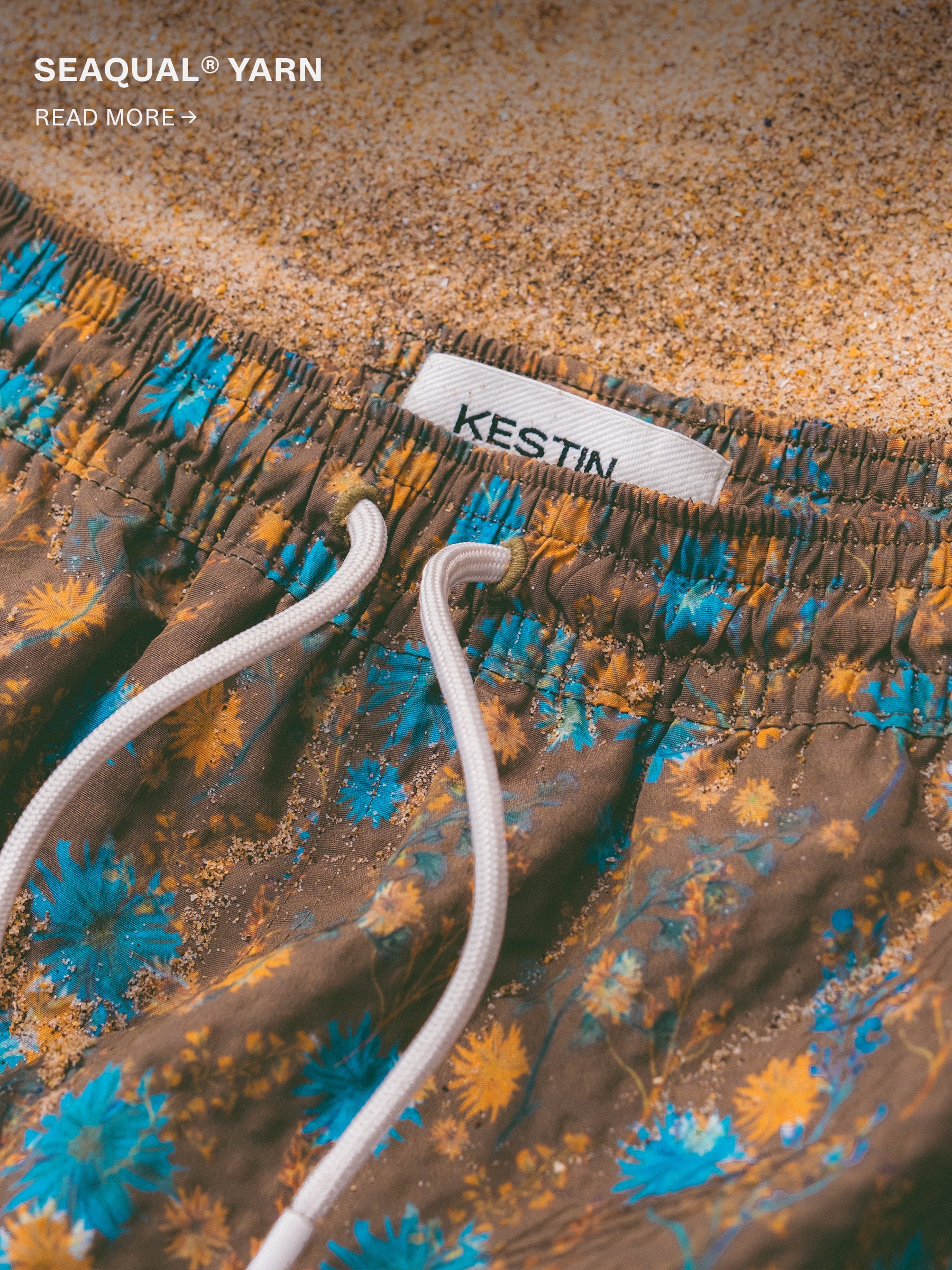 A pair of green floral swimming trucks, lying on some sand.