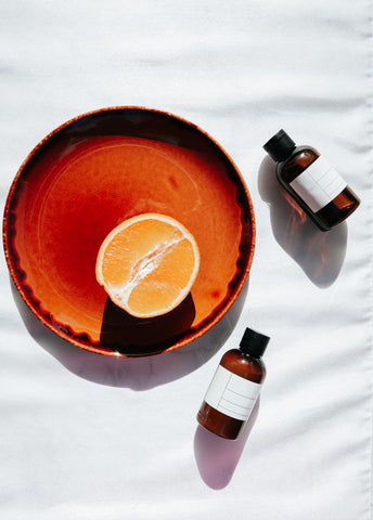 Plate with half an orange and 2 small brown glass bottles on a white cloth