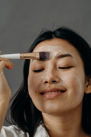 Chinese girl applying light pink clay mask with a brush and smiling