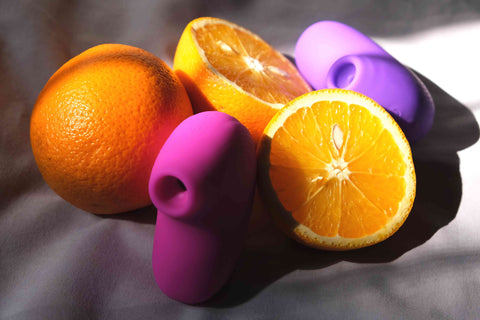 visual of two pink and purple vibrator for women kept on a sheet with three oranges