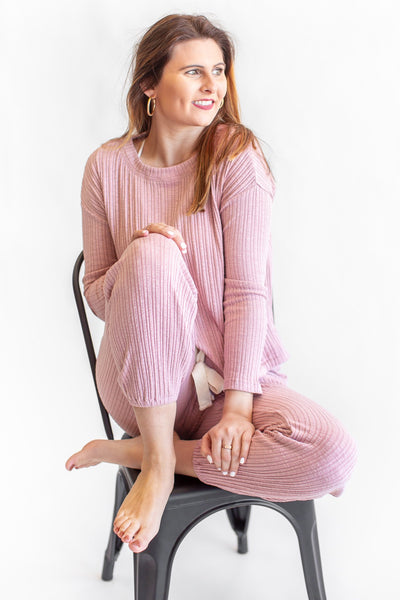 Girl Sitting In Chair Dressed in Pink Lounge Set Against White Background