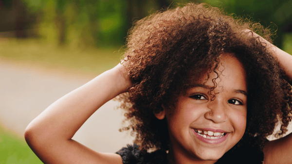 American african little girl smiling touching her hair outdoors