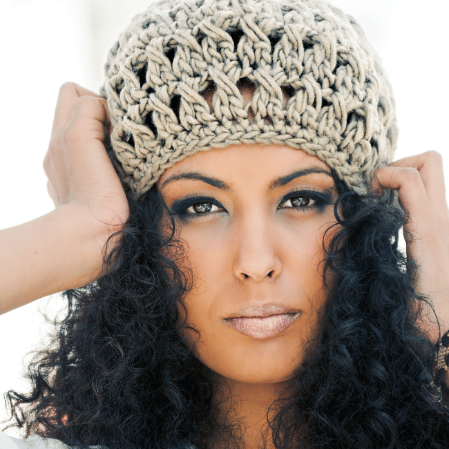 African american woman wearing crochet beanie holding her head