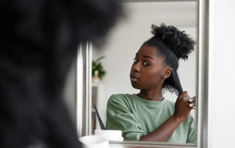 Medium shot young curly black woman arranging hair in front of the mirror