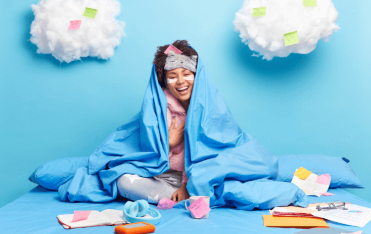 Positive sincere dark skinned woman laughs with blanket on