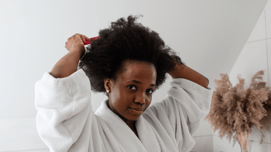 African american woman wearing a white bathrobe detangling her hair
