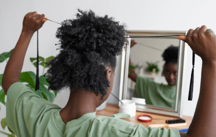 Side view young curly haired black woman arranging hair in mirror