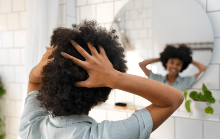 Young black person taking care of afro hair facing a mirror