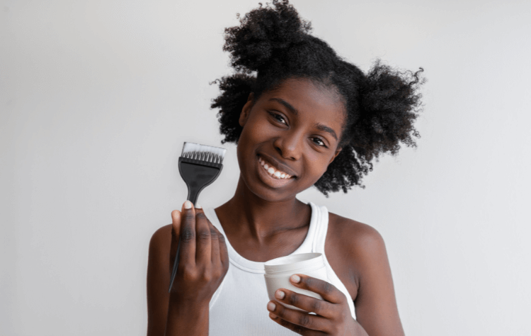 front view smiley curly black woman holding a brush and a hair product
