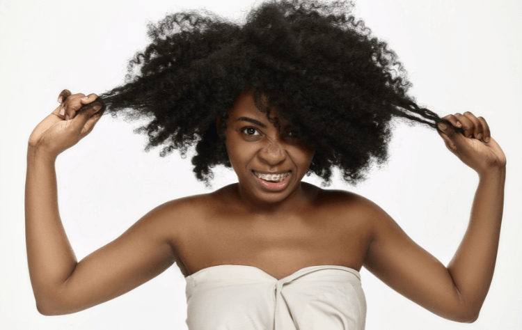 portrait young black african american woman smiling with braces pulling her hair