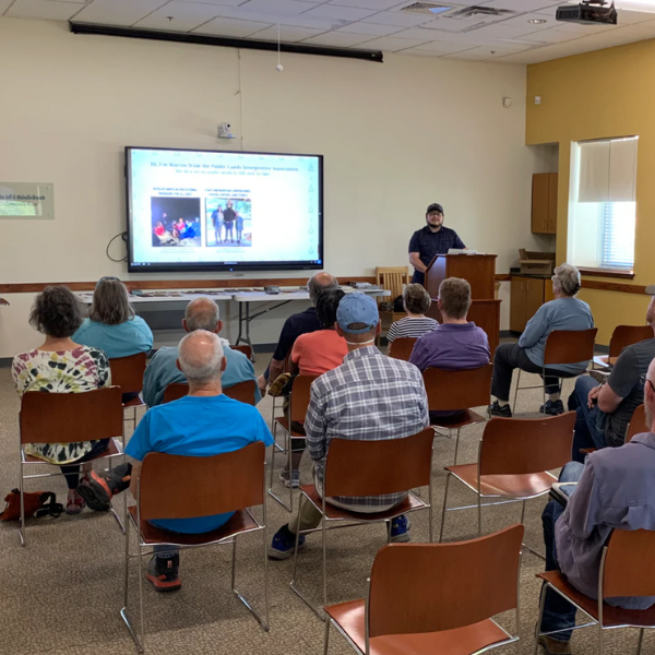 Person giving a presentation on a tv screen to a crowd seen from behind.