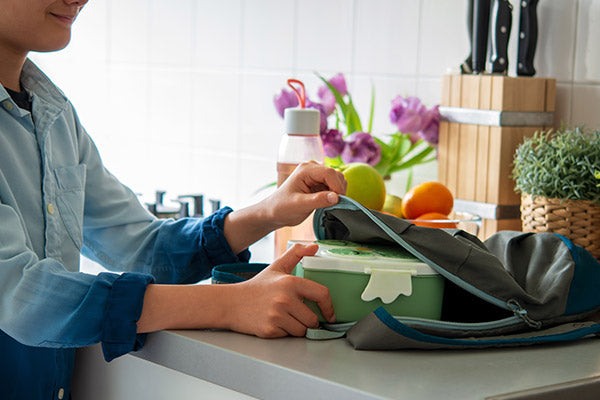 Kid reaching for his lunch box on the kitchen counter.