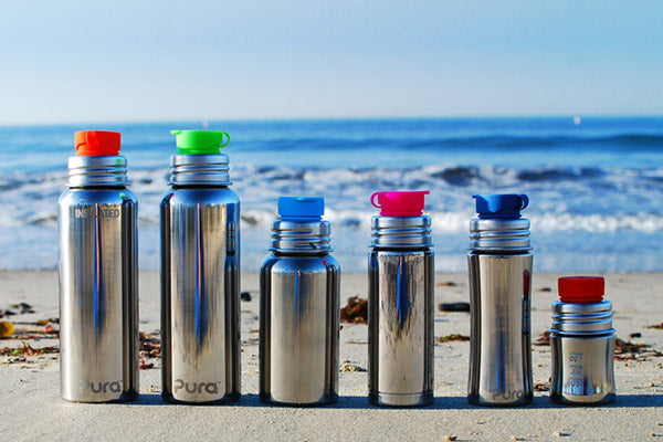 Pura Stainless plastic-free bottles lined up on a beach.