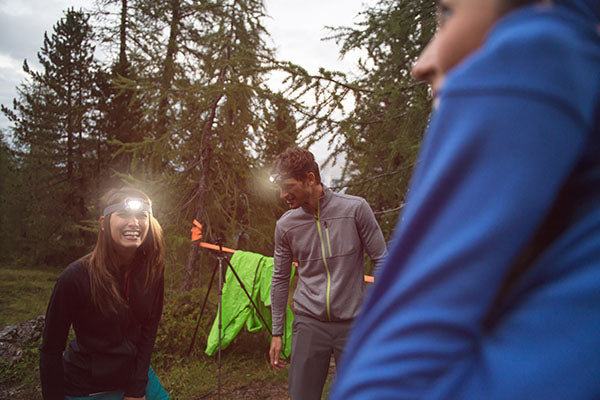 Smiling woman wearing a headlamp while camping with friends.
