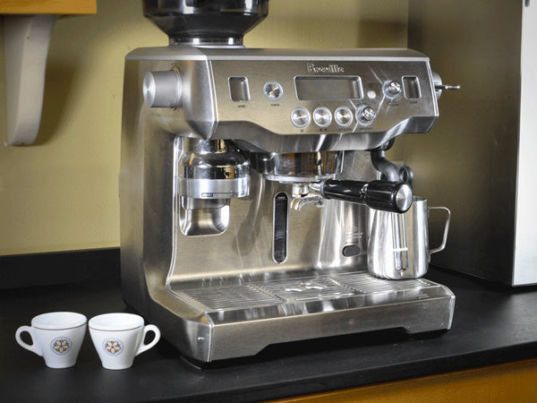 a fully equipped Breville espresso machine sits on a counter beside portafilter and ristretto cups