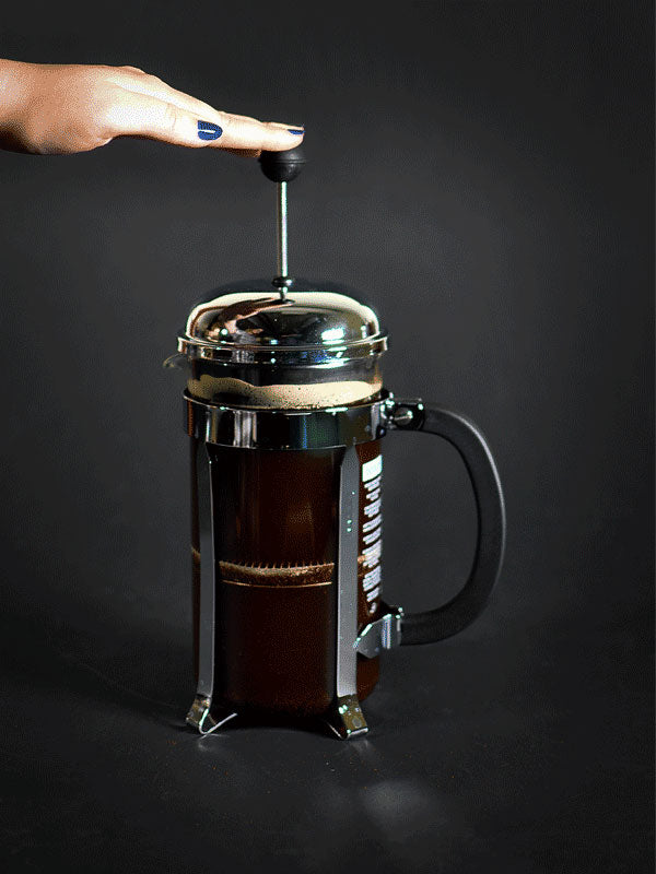 How to use a French Press - A photograph of a hand pressing the plunger of a French Press.