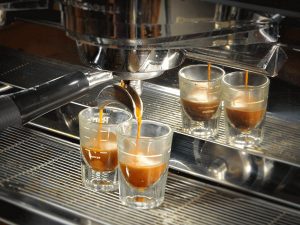 two shot glasses collect the espresso that drips from the portafilter on an espresso machine