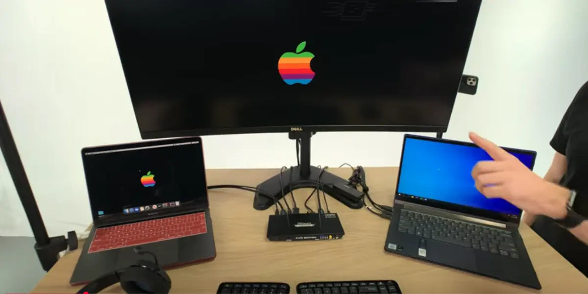 MacBook and Windows laptop connected to one monitor using a KVM switch, showing 2 computer setup with shared peripherals.