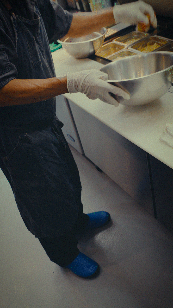Person in kitchen with gloves holding bowl and utensils.