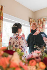 Image of Janna founder and makeup artist from Behind the Blush preparing a bride for her 2020 wedding at a home in Edmonton, Alberta, Canada. Image also features florals from FaBLOOMosity. Photo Credit: Sarah Mavro Photography