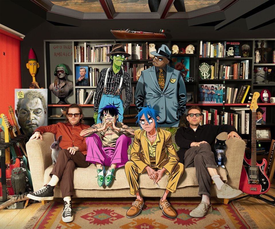 Gorillaz the band sitting on a sofa in a room full of music, with creators Damon Albarn and Jamie Hewlett