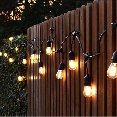 String of festoon lights with black cord and exposed bulbs hanging on outdoor fence