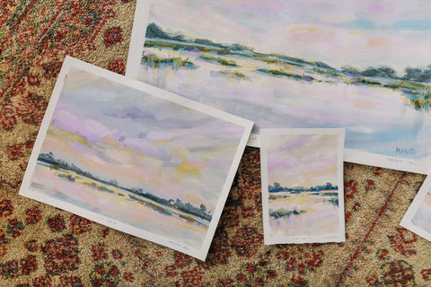 Coastal watercolor paintings layered together on a rug.