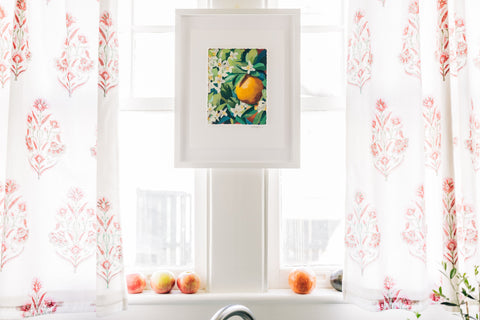 Painting of oranges hanging in-between two kitchen windows.