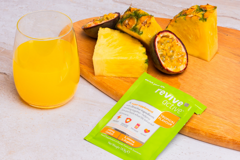 Revive Active Tropical sachet on kitchen counter with a chopping board, tropical fruits and green revive active sachet and drink