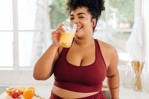 A plus-sized woman wearing activewear while drinking a glass of orange juice.