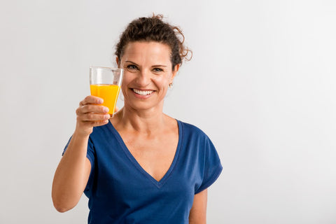 A smiling, attractive, middle-aged woman wearing blue, holding a glass of orange drink