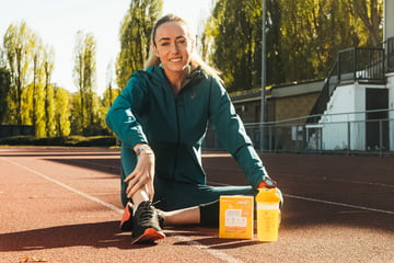 Eilish McColgan, British & European record-holder and 3-time Olympian, is sitting on a running track next to a Zest Active box and full shaker.