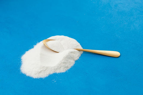 Gold coloured spoon in a pile of collagen powder, against a blue background