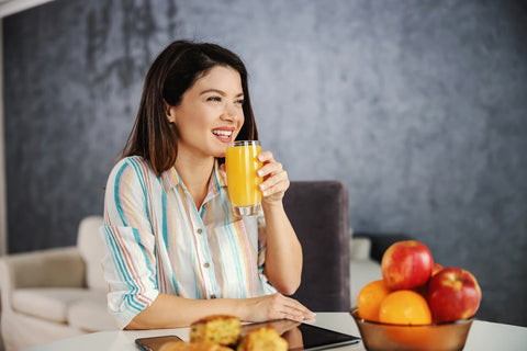Smiling woman, sitting at the table eating breakfast while drinking a glass of orange juice