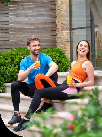 A young man and woman in sportswear, sitting on some steps, smiling, holding a glass or Zest Active 