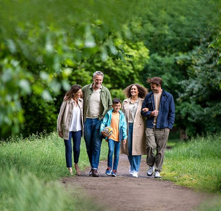 A group of five people walking outdoors, there is a young couple, an older couple and a young boy holding a rugby ball. 