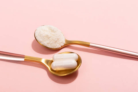 Two metal spoons facing opposite directions, one spoon containing two collagen capsules, the other containing collagen powder.