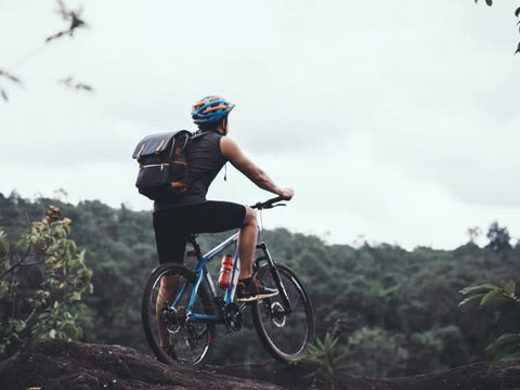 A man mountain biking on uneven terrain, overlooking hilly landscape covered in trees. 
