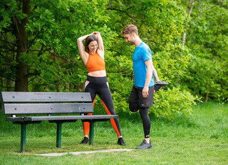 Two runners stretching next to a bench