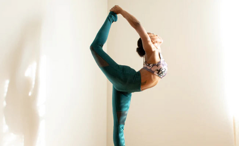 A woman in an advanced yoga pose with the sun shining through a window, onto her face and body.