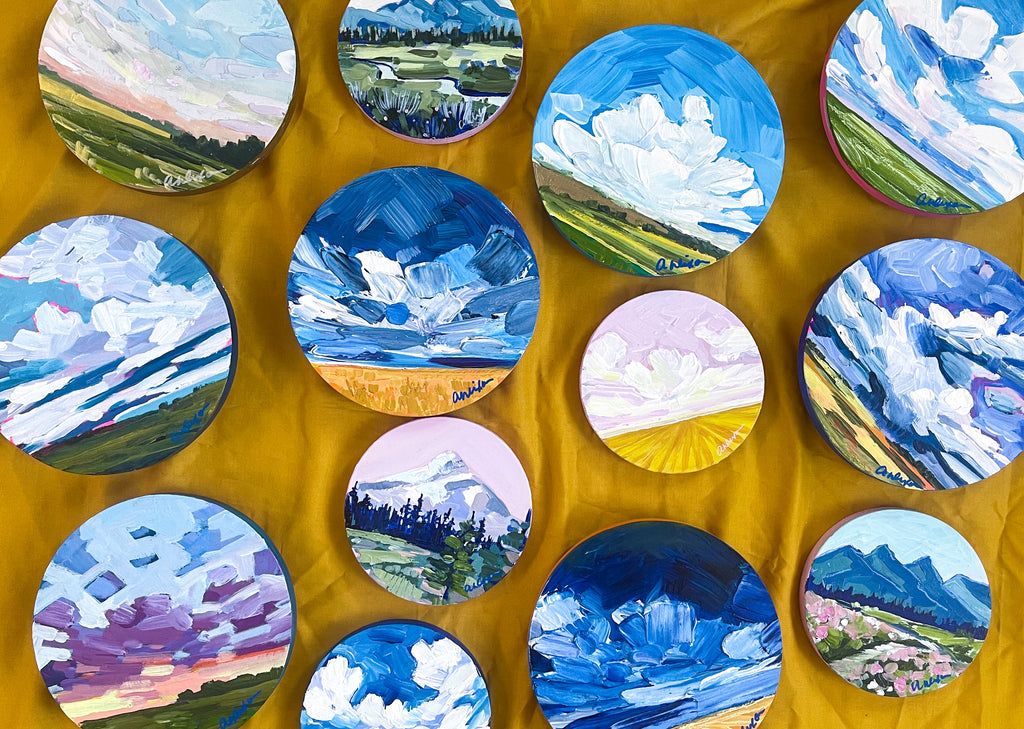 A collection of small round paintings of prairies, mountains, and seascapes.