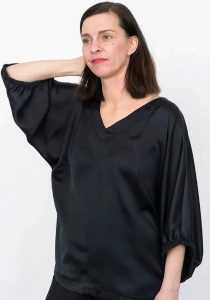  a white woman wearing a v neck top in a black silky fabric