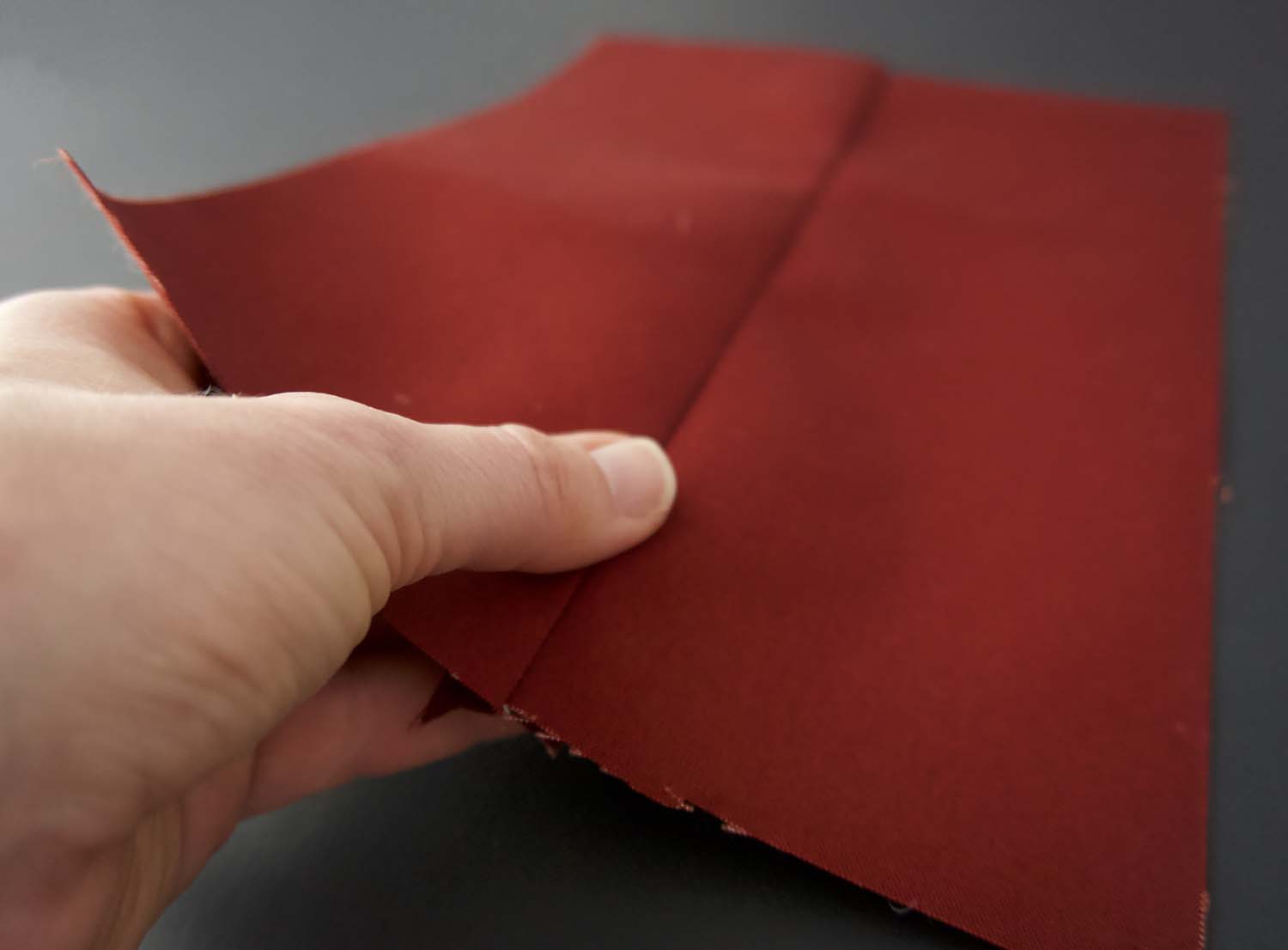 a picture of a thumb pressing down a seam on some dark red oilskin