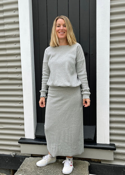 white lady wearing a light grey jumper and matching straight skirt