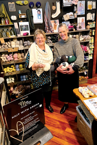 Emma and Tracey standing together in front of the a wall of different coloured yarn