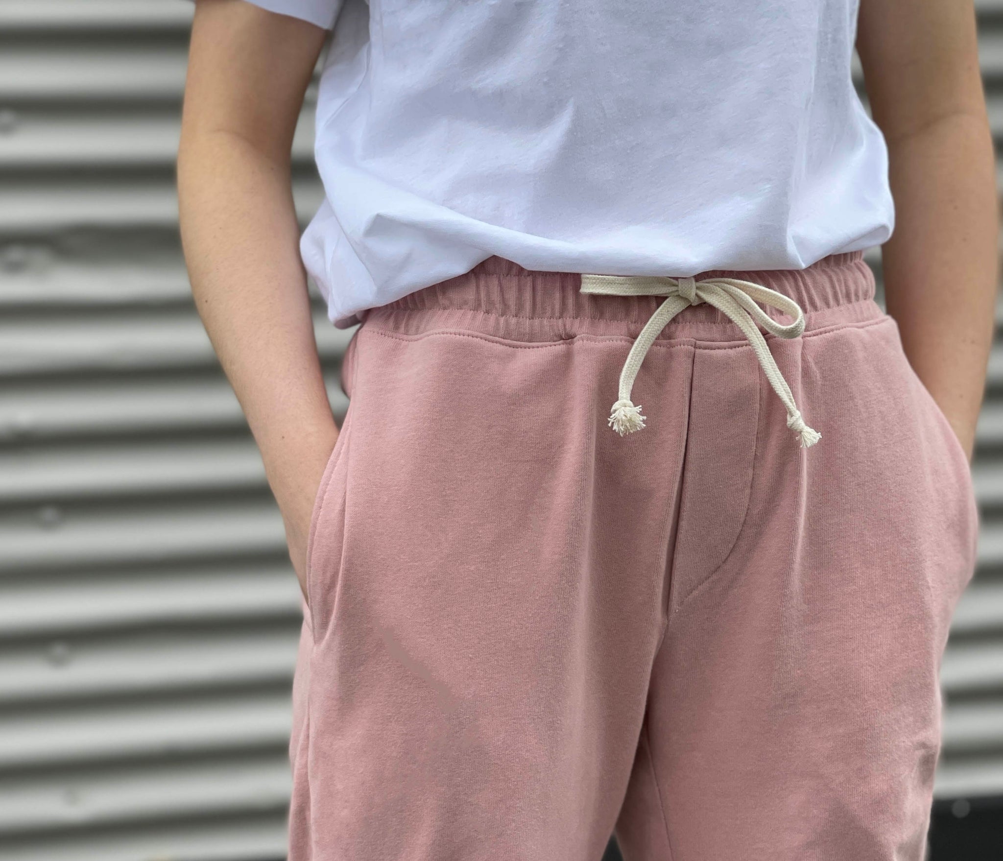 a close up of the waist band of some tracksuit pants wearing a white tee with pink bottoms. there is a cream tie in the waist band