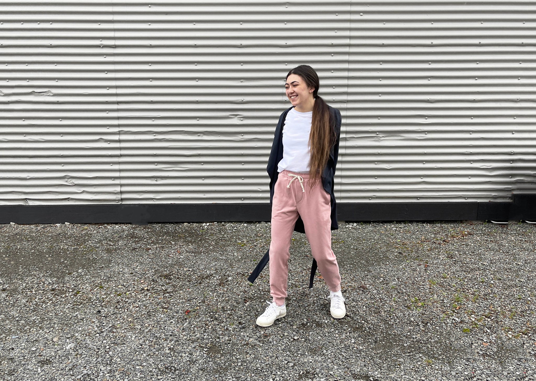 a girl standing in front of a corrugated iron building wearing a grey cardigan, white t-shirt and pink tula pants from papercut patterns 