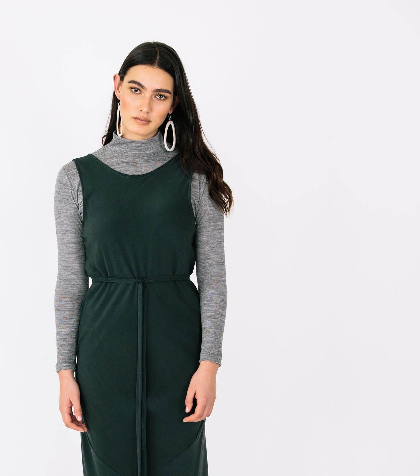 a picture of a white woman with long dark hair wearing a dark green dress layered over the top of a grey turtleneck