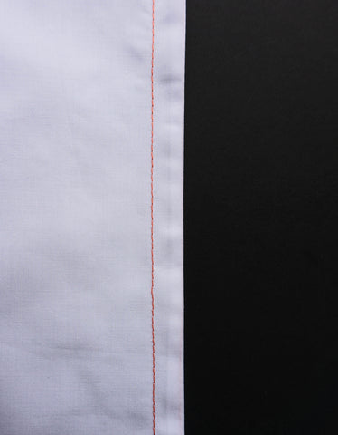 a white pice of fabric to the right hand side with orange french seam on the right hand edge with a black background